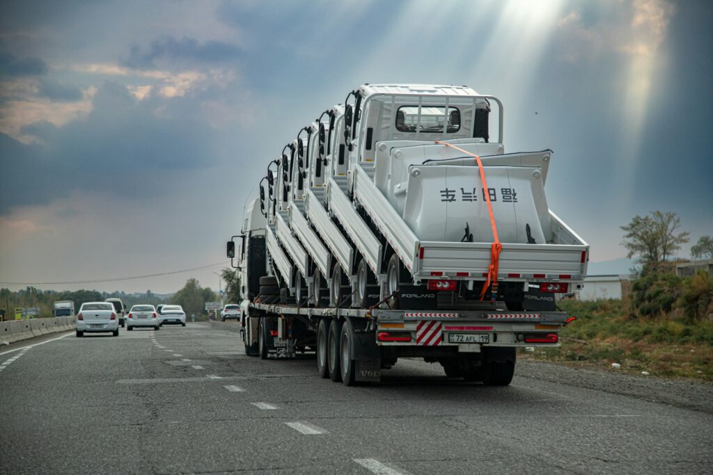 A flatbed truck carrying several stacked white truck cabs on a highway under a cloudy sky