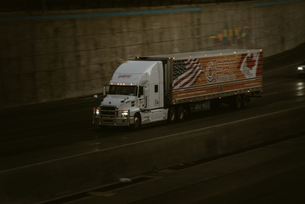 A white semi-truck driving along a highway beside a concrete retaining wall