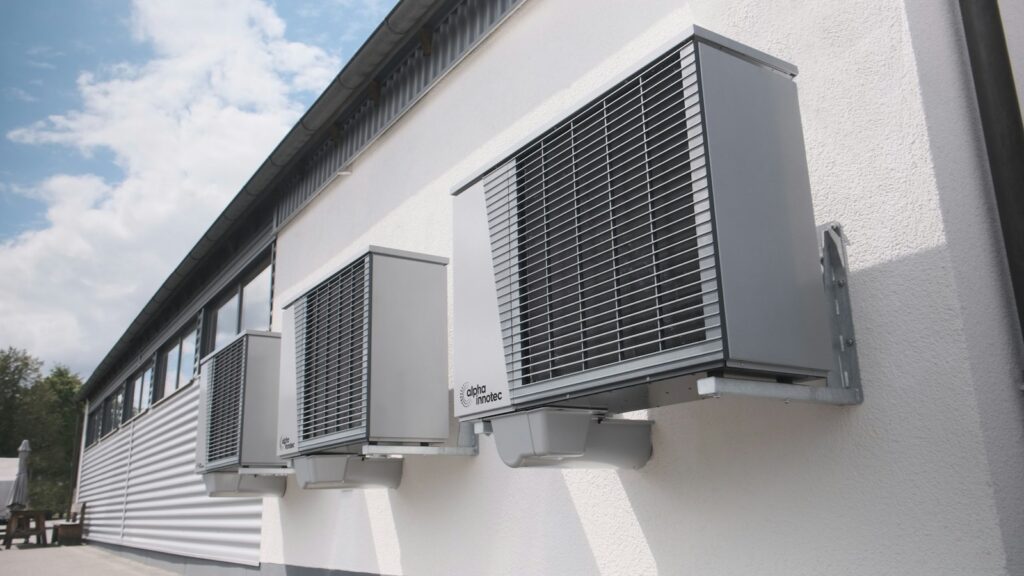 Three gray air conditioning units mounted on a white wall